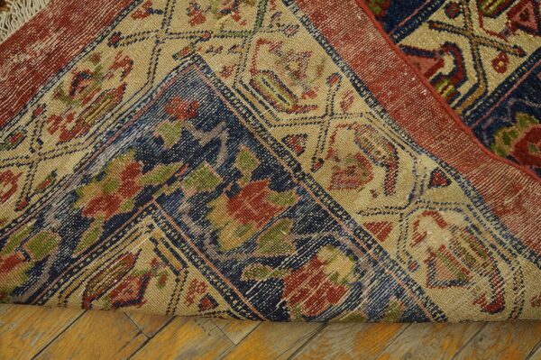 A patterned rug with red, navy, and beige elements is rolled back on light wood flooring.