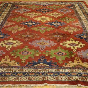Reddish-brown rug with multi-colored geometric designs and intricate borders on a wood floor.