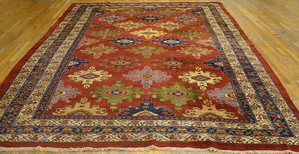 Reddish-brown rug with multi-colored geometric designs and intricate borders on a wood floor.