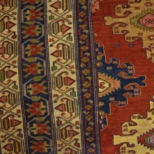 Intricate rug pattern featuring red, navy, and tan colors with geometric and stylized floral motifs.
