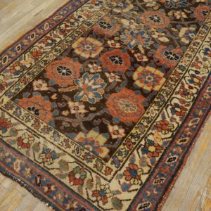 A detailed floral patterned rug in rust, blue, and cream lies on worn light hardwood flooring.