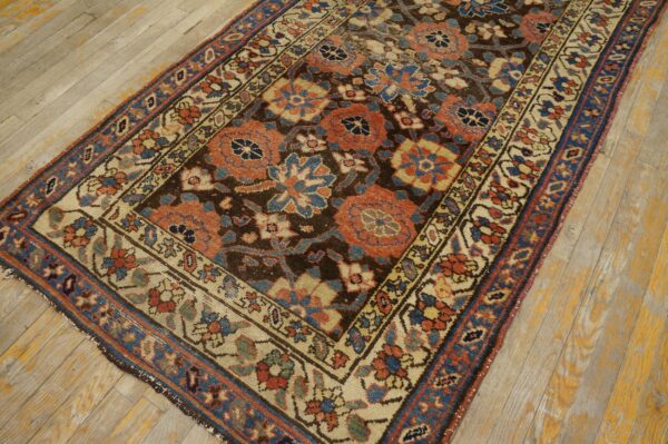 A detailed floral patterned rug in rust, blue, and cream lies on worn light hardwood flooring.