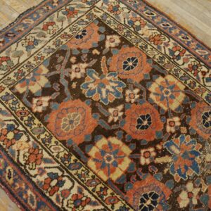 Traditional rug with coral and blue floral motifs and a dark brown ground on light wood planks.