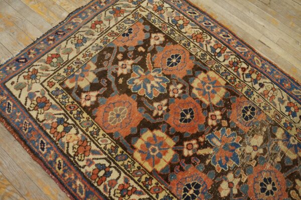 Traditional rug with coral and blue floral motifs and a dark brown ground on light wood planks.