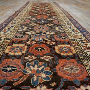 Low pile runner rug featuring terracotta, blue, and cream geometric patterns on a brown field and wood floor.