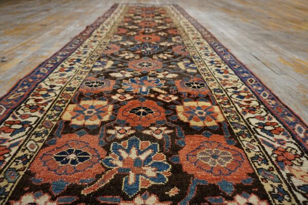 Low pile runner rug featuring terracotta, blue, and cream geometric patterns on a brown field and wood floor.