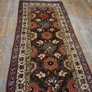 Runner rug featuring rust, navy, and cream floral patterns on a dark brown field over worn wood floorboards.