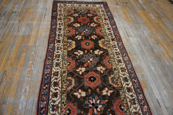 Runner rug featuring rust, navy, and cream floral patterns on a dark brown field over worn wood floorboards.