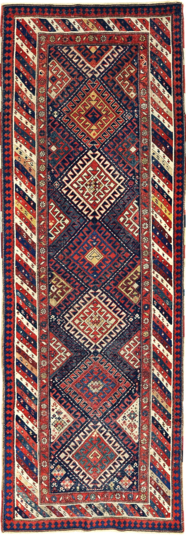 Narrow runner rug displaying complex geometric patterns, nested diamonds, and diagonal stripes in red, navy, and cream.