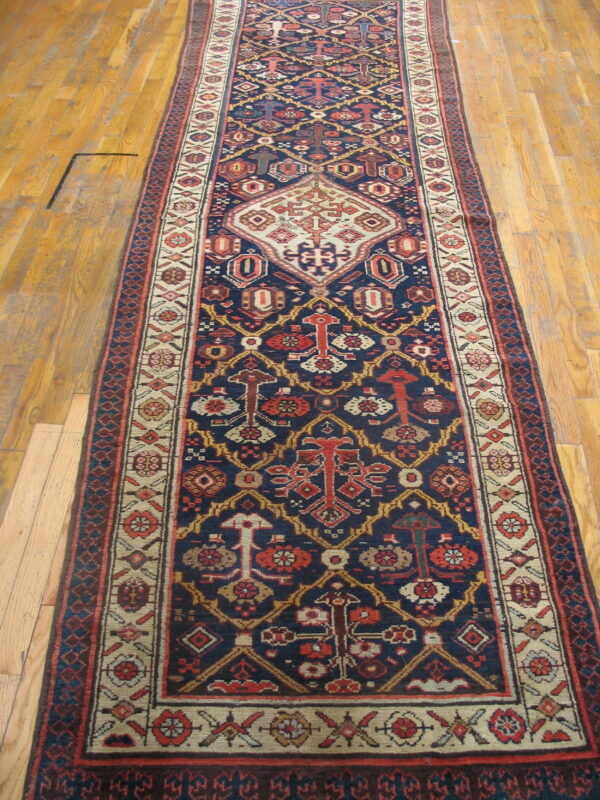 Navy blue runner rug featuring geometric red and cream tribal medallions sits on light hardwood floors.