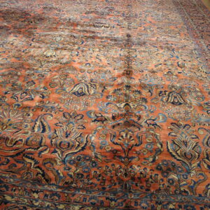 The expansive rug features an ornate pattern in orange, dark blue, and tan on light hardwood flooring.