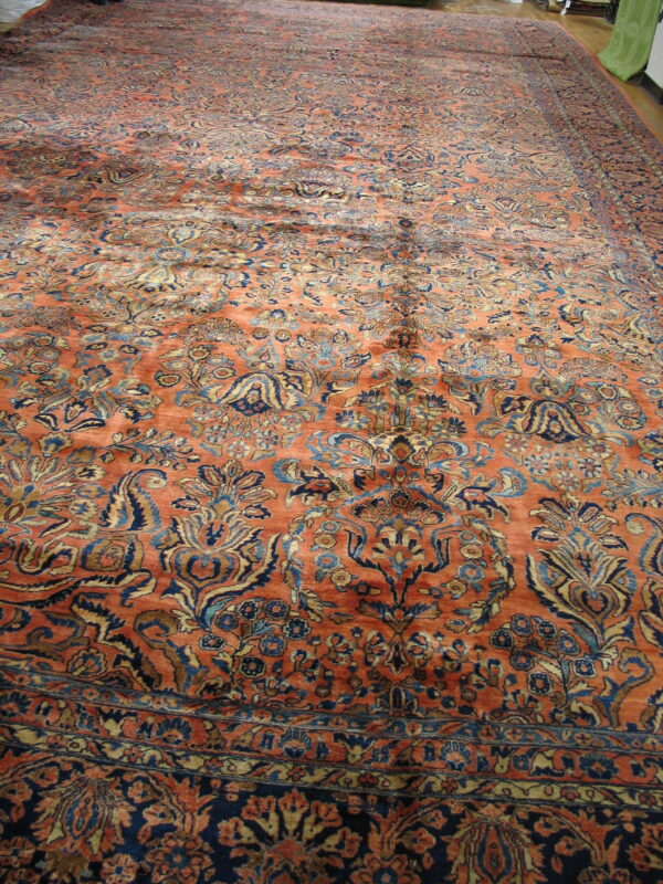 The expansive rug features an ornate pattern in orange, dark blue, and tan on light hardwood flooring.