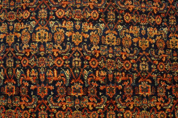 High-pile rug surface showing a dense traditional pattern in navy, rust red, and orange.