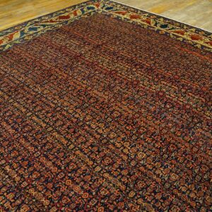A dense patterned rug in navy blue, rust, and gold lies on light hardwood flooring.