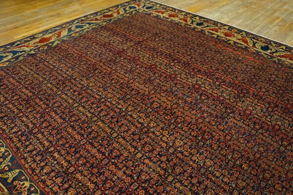 A dense patterned rug in navy blue, rust, and gold lies on light hardwood flooring.