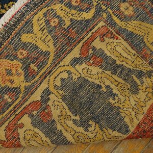 A folded rug displays its dark blue, red, and gold patterned pile and tightly woven backing on wood floor.