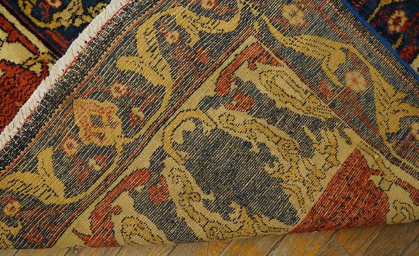A folded rug displays its dark blue, red, and gold patterned pile and tightly woven backing on wood floor.