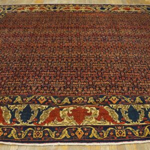 Red and navy patterned rug with a pictorial border featuring stylized figures, displayed on wood flooring.
