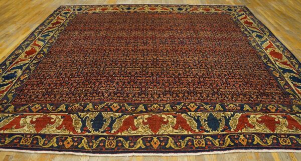 Red and navy patterned rug with a pictorial border featuring stylized figures, displayed on wood flooring.