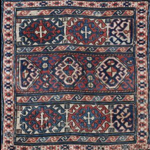 Low-pile rug featuring complex geometric patterns with crosses and diamonds in red, indigo, and ivory.