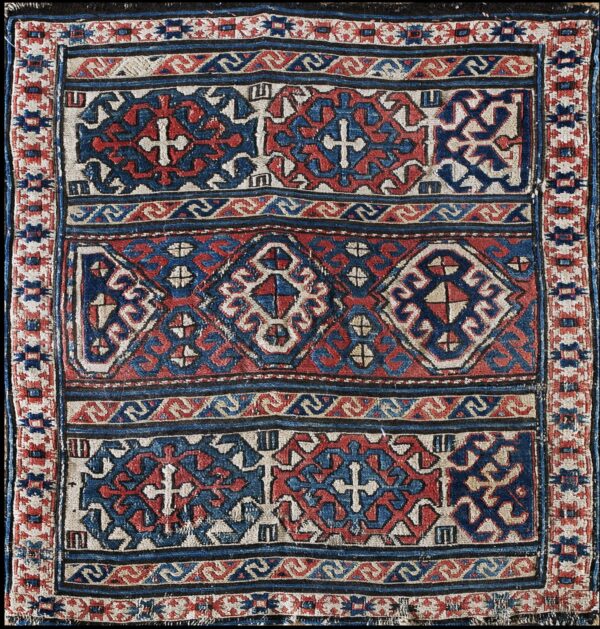 Low-pile rug featuring complex geometric patterns with crosses and diamonds in red, indigo, and ivory.