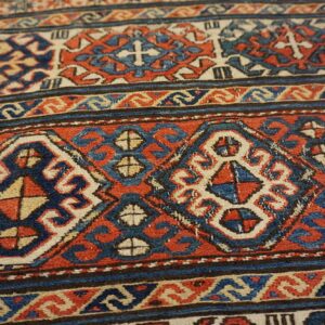 Low-pile tribal rug detail with deep red, indigo, and ivory geometric patterns and thick stripes.