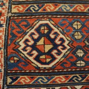 Close-up of a rust, indigo, and cream geometric rug pattern showing a central diamond motif and borders.