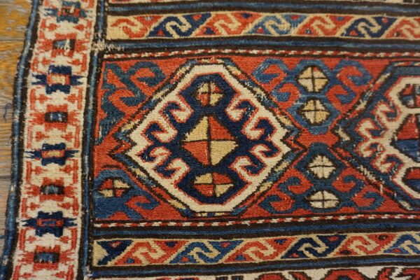 Close-up of a rust, indigo, and cream geometric rug pattern showing a central diamond motif and borders.