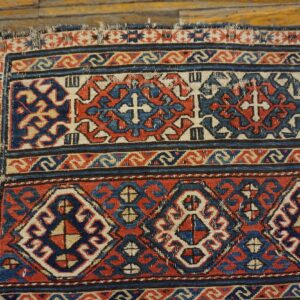 Geometric red, blue, and beige rug with repeating medallions and crosses on rustic hardwood flooring.