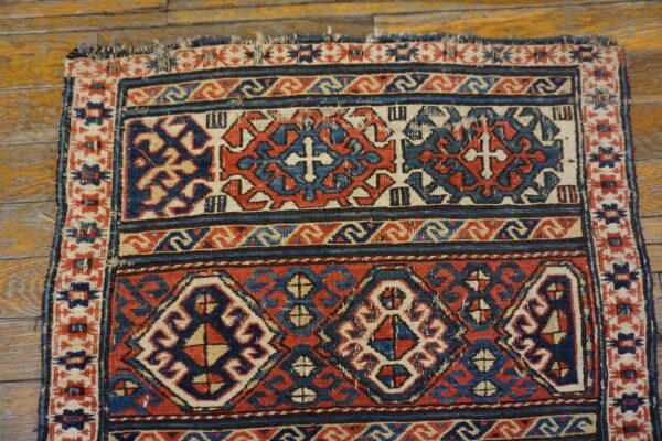 Geometric red, blue, and beige rug with repeating medallions and crosses on rustic hardwood flooring.