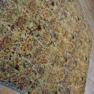 Large low-pile rug featuring a dense pattern of yellow, pink, maroon, and blue flowers on wooden floor.