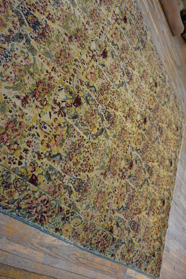 Large low-pile rug featuring a dense pattern of yellow, pink, maroon, and blue flowers on wooden floor.