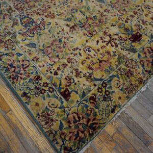 Low-pile rug with dense floral pattern in yellow, pink, and blue rests on distressed hardwood flooring.