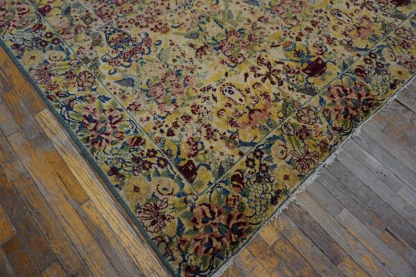 Low-pile rug with dense floral pattern in yellow, pink, and blue rests on distressed hardwood flooring.