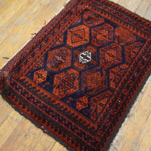 Small dark red and navy rug with geometric medallions and thick borders on light wooden floors.