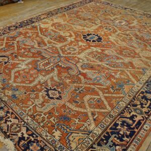 Rust-colored rug featuring a complex navy, cream, and blue geometric medallion pattern on hardwood.