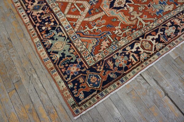 Rust rug with navy and beige border featuring complex geometric patterns rests on distressed gray wood planks.