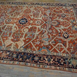 Ornate red-orange rug with navy blue and ivory geometric patterns rests on weathered wood planks.