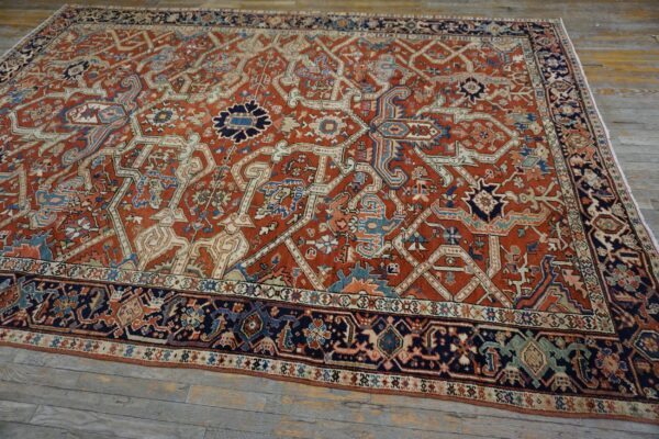 Ornate red-orange rug with navy blue and ivory geometric patterns rests on weathered wood planks.