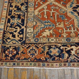 Rust and navy traditional rug corner with fringe displayed on textured wood plank flooring.