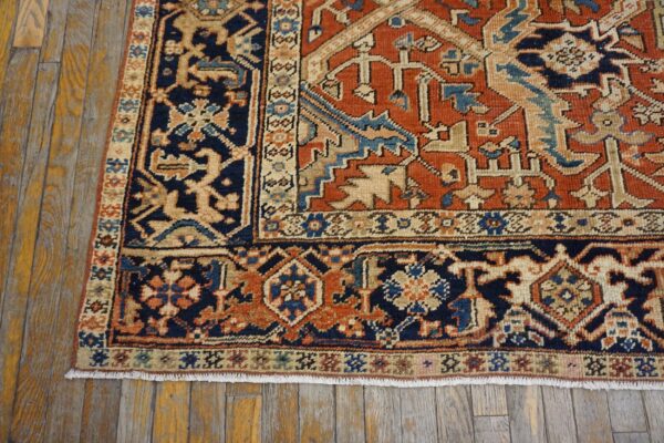 Rust and navy traditional rug corner with fringe displayed on textured wood plank flooring.