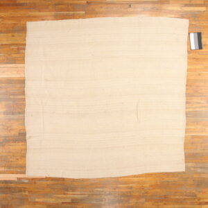Beige rectangular flatweave rug on a distressed wooden plank floor with a calibration card nearby.