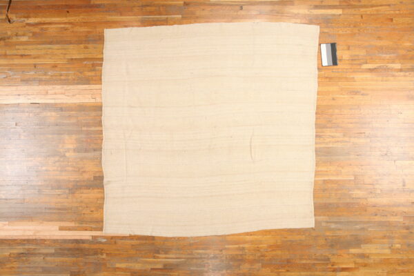 Beige rectangular flatweave rug on a distressed wooden plank floor with a calibration card nearby.