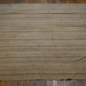 A beige flatweave rug featuring horizontal stripes rests on a dark plank wood floor.