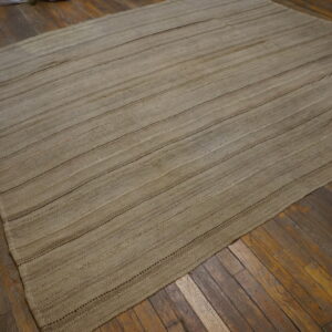 Natural khaki flatweave rug with prominent horizontal stitching rests on distressed dark wood flooring.