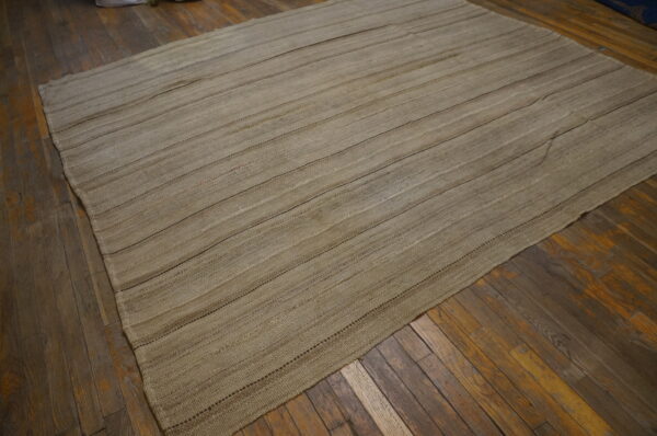 Natural khaki flatweave rug with prominent horizontal stitching rests on distressed dark wood flooring.