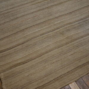 Rustic flatweave rug in neutral earth tones featuring subtle horizontal striping on distressed wood planks.