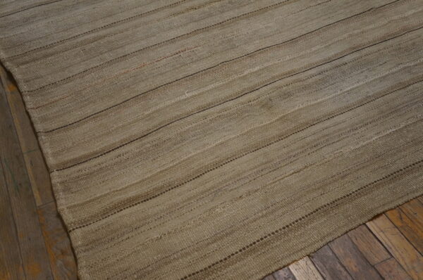 Rustic flatweave rug in neutral earth tones featuring subtle horizontal striping on distressed wood planks.