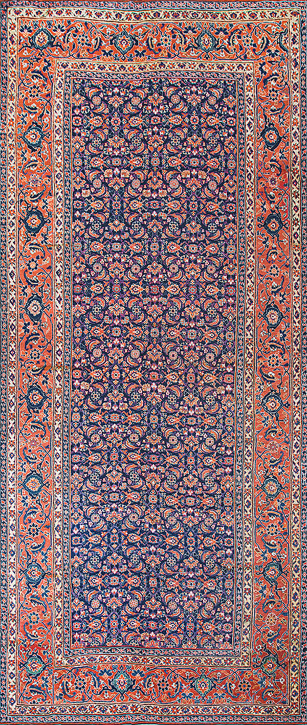 Close-up of a densely patterned rug featuring red, navy, and gold colors on rustic wood floorboards.