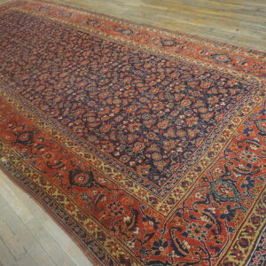 A large low-pile rug with a dark field and dense floral pattern lies on distressed gray wood planking.